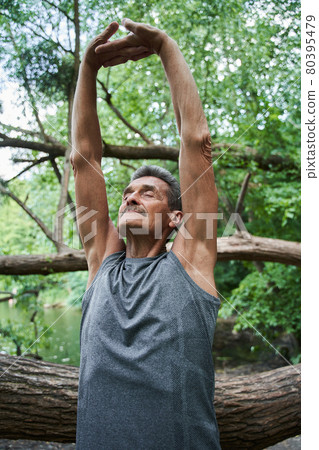 Senior man stretching arms and closed eyes while doing morning exercises at fresh air Senior man stretching arms and closed eyes while doing morning exercises at fresh air 80395479