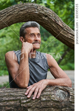 Elderly man standing near the tree and looking away with pleasure Elderly man standing near the tree and looking away with pleasure 80395535