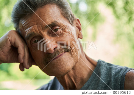 Man looking at the camera with pleasure smile while leaning at the trunk of the tree 80395613