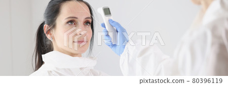 For doctor in protective suit, body temperature is measured with thermometer after work shift 80396119