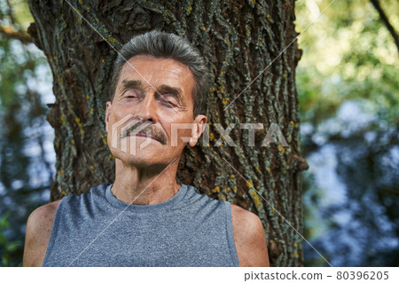 Man leaning with closed eyes at the tree trunk and absorbs good energy 80396205