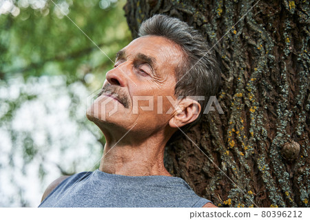 Man leaning with closed eyes at the tree trunk and absorbs good energy 80396212