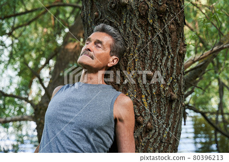 Man keeping eyes closed and relaxing in the forest while laying at the trunk 80396213