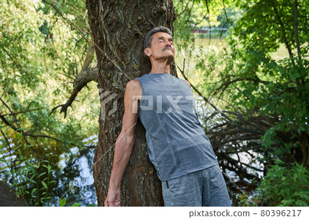 Man keeping eyes closed and leaning at the tree trunk while relaxing and meditating 80396217