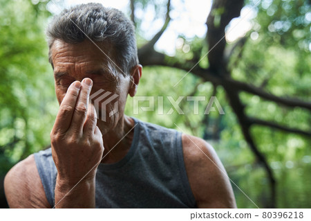 Senior man practicing breathing yoga pranayama while sitting at the mat outdoors 80396218