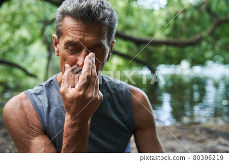 Man keeping his eyes closed and doing breathing exercise while closes nostril with finger 80396219