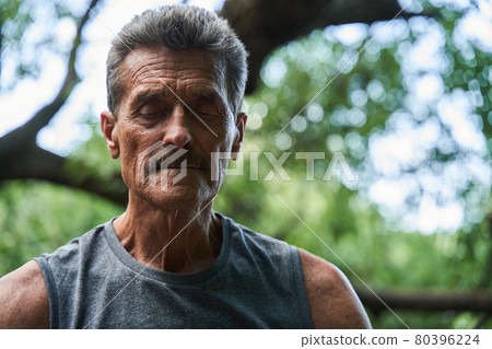 Mature man keeping his eyes closed and enjoying of the nature while meditating 80396224