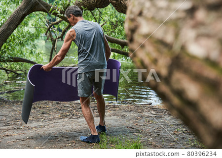 Man putting yoga mat at the ground while preparing to the training at the open air Man putting yoga mat at the ground while preparing to the training at the open air 80396234