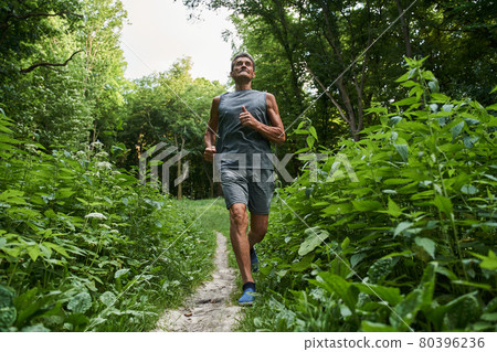 Male running with concentration in the summer park around the trees Male running with concentration in the summer park around the trees 80396236