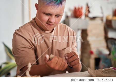 Boy with colored hair holding clay at the hands and examining it during the master class 80396284