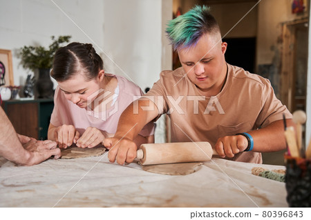 Down syndrome boy with special needs rolling out with the pin clay 80396843