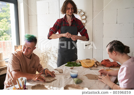Sculptor wearing apron smiling while teaching his master class for the people 80396859