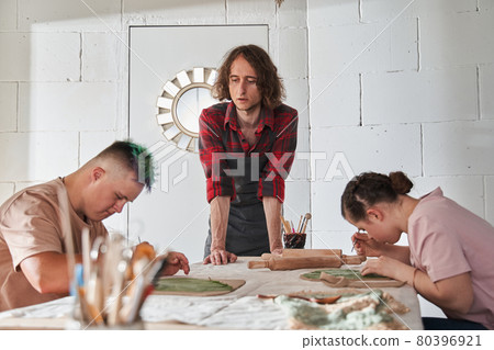 People with special needs making plate of the clay under the supervision of a mentor 80396921