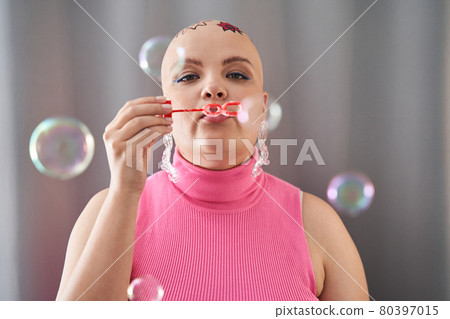 Bald girl blowing soap blebs with enjoyment while spending time at home 80397015