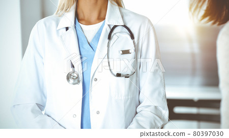 Unknown woman-doctor and patient in sunny hospital. Physician controls medication history records and exam results while using clipboard, close-up 80397030