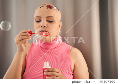 Bald girl blowing soap blebs with enjoyment while spending time at home Bald girl blowing soap blebs with enjoyment while spending time at home 80397399