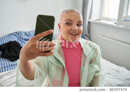 Bald woman making selfie at her smartphone while creating new image and recovering Bald woman making selfie at her smartphone while creating new image and recovering 80397474