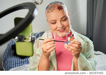Woman sitting in front of the smartphone on tripod and applying creative pattern to her head 80397485
