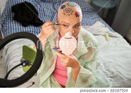Blogger with colored patterns at head preparing makeup in front of smartphone 80397504