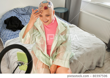 Woman sitting on the bed and looking at the camera of a smartphone on tripod 80397506