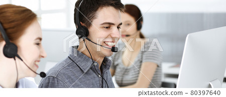 Casual dressed young man using headset and computer while talking with customers online. Group of operators at work. Call center Casual dressed young man using headset and computer while talking with customers online. Group of operators at work. Call center 80397640