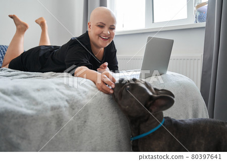Bald woman feeding her dog while laying at the bed and working Bald woman feeding her dog while laying at the bed and working 80397641