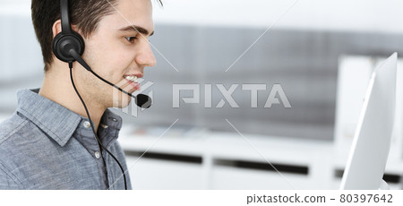 Casual dressed young man using headset and computer while talking with customers online. Call center, business concept Casual dressed young man using headset and computer while talking with customers online. Call center, business concept 80397642