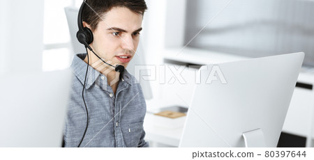 Casual dressed young man using headset and computer while talking with customers online. Call center, business concept Casual dressed young man using headset and computer while talking with customers online. Call center, business concept 80397644