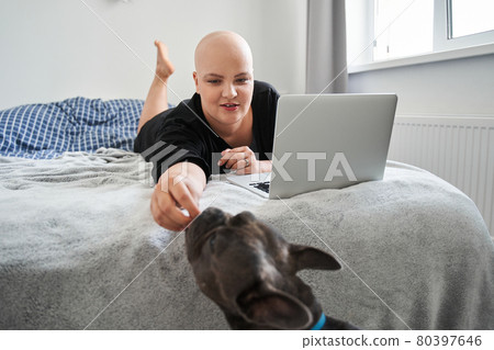 Bald woman feeding her dog while laying at the bed and working Bald woman feeding her dog while laying at the bed and working 80397646