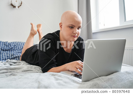 Woman laying at her stomach at the bed and looking at the digital screen of her laptop 80397648