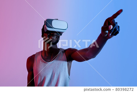 Exercising with virtual reality. Young black guy in VR headset touching button on imaginary screen in neon light, mockup Exercising with virtual reality. Young black guy in VR headset touching button on imaginary screen in neon light, mockup 80398272