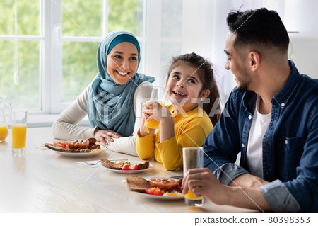 Happy islamic family with little daughter eating tasty breakfast together in kitchen Happy islamic family with little daughter eating tasty breakfast together in kitchen 80398353