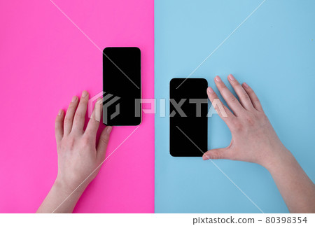Female hands touching two smartphones with blank screens on blue and pink backgrounds, top view, flat lay 80398354
