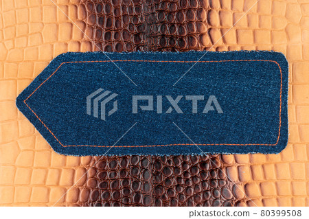 Arrow made of denim is lying on a brown crocodile skin. With space for design, text place. Arrow made of denim is lying on a brown crocodile skin. With space for design, text place. 80399508