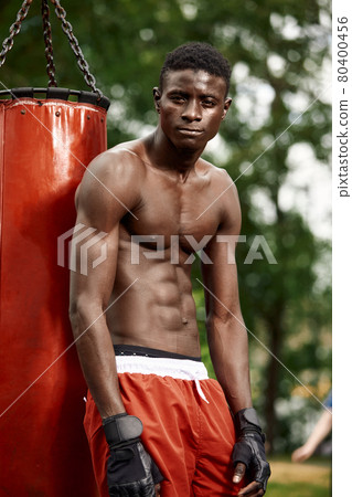 Muscular black professional boxer sweating in gloves boxing training outdoors, young african american boxer exercising on the street playground 80400456