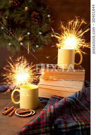 tea cups with sparkle and christmas background, ceramic cup with bright light inside, books and blanket with scrolls and cinnamon 80401844