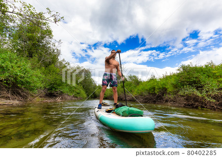Adventurous Hispanic Adult Athletic Man paddle boarding 80402285