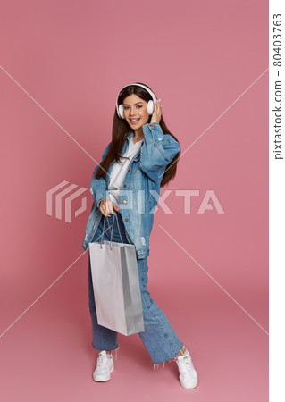 happy beautiful woman in headphones holding shopping bags 80403763