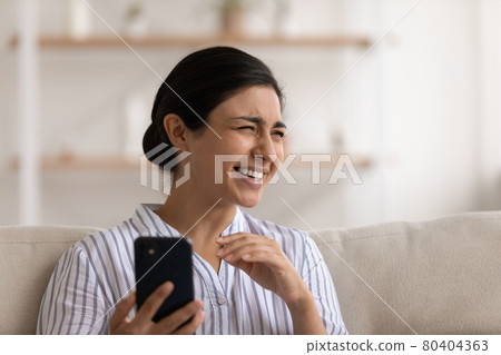 Close up excited Indian millennial woman holding smartphone, having fun 80404363