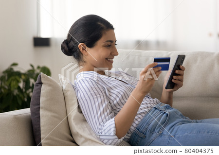 Side view smiling Indian woman paying online by credit card Side view smiling Indian woman paying online by credit card 80404375