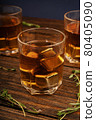 Glass with whiskey and metal ice cubes on a wooden table close-up. 80405090