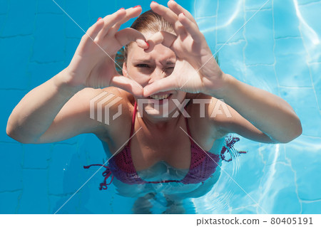 Laughing young woman in the pool shows the sign of the heart wit 80405191