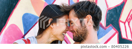 Young couple in love laughing together at Berlin wall, Germany, Europe travel. Portrait of happy multiracial people, Asian woman, Caucasian man kissing. Banner panorama on graffit background. 80405226