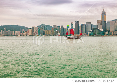 Hong Kong city view from Kowloon at sunset with red sail junk boat in river. Asia travel skyline background landscape. Hong Kong city view from Kowloon at sunset with red sail junk boat in river. Asia travel skyline background landscape. 80405242