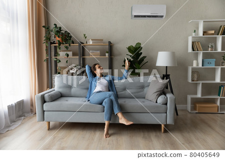 Woman relax on couch holding remote controller turns on airconditioner Woman relax on couch holding remote controller turns on airconditioner 80405649