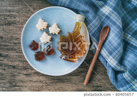 Maple syrup top view of organic natural product from Canada. Maple leaf shape bottle, soft candy and hard candy taffy on rustic wooden kitchen table and spoon for cooking Maple syrup top view of organic natural product from Canada. Maple leaf shape bottle, soft candy and hard candy taffy on rustic wooden kitchen table and spoon for cooking 80405657