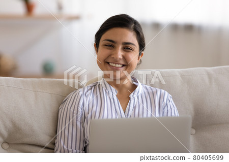 Head shot portrait smiling Indian woman using laptop on couch Head shot portrait smiling Indian woman using laptop on couch 80405699