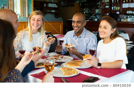 Cheerful friends enjoying dinner with pizza in cozy restaurant 80410039
