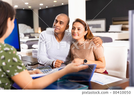 Young happy hispanic couple consulting with furniture saleswoman when choosing new mattress in store Young happy hispanic couple consulting with furniture saleswoman when choosing new mattress in store 80410050
