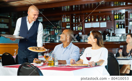 Polite waiter bringing ordered pizza to couple visited restaurant for lunch 80410053